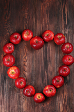 Ripe red apples in shape of heart on wooden background