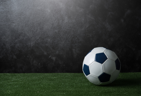 Soccer ball on green grass against black cement wall Stock Photo