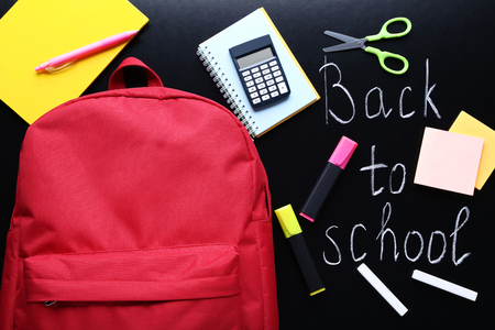 Red backpack with school supplies on black chalkboard