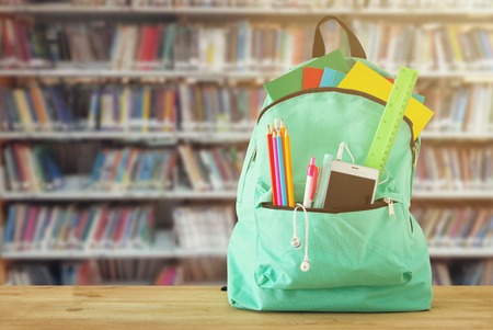 School bag with stationery and notebooks in front of shelves with books library back to school concept