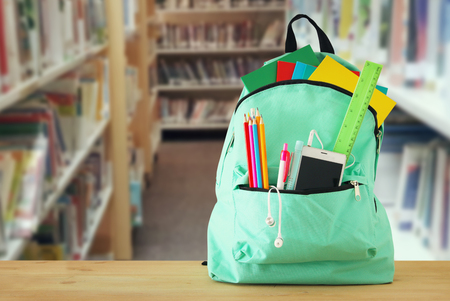 School bag with stationery and notebooks in front of shelves with books library back to school concept Stock Photo