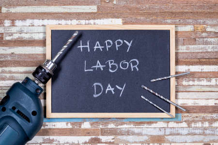 Chalk board with text happy labor day with electronics drills on a rusty wooden table Stock Photo