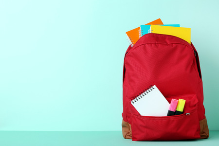 Red backpack with school supplies on mint background