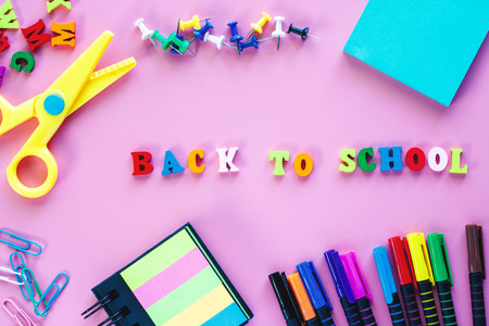 School supplies with coloured pen scissors binder clip push pins paper note sticky note and wooden text back to school on pink background for education concept