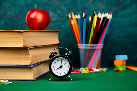 Back to school supplies books and red apple on green background still life with alarm clock copy space