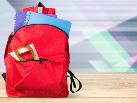 Colorful school supplies in backpack on blackboard Stock Photo