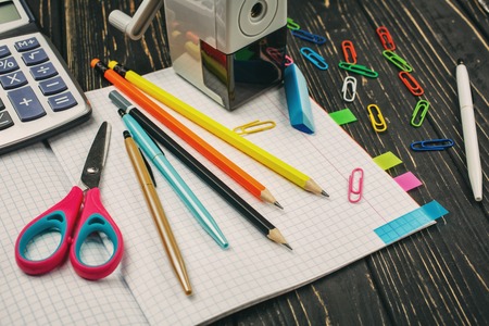 Bright items for a school on a wooden table pens pencils scissors a calculator and an elastic on an open notebook Stock Photo