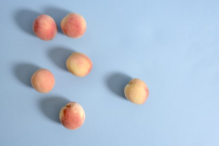 Whole ripe beautiful peaches on blue background with shadows