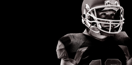 American football player standing with rugby helmet against black background