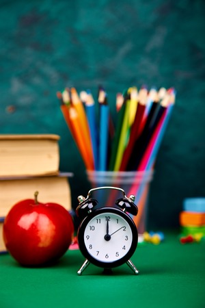 Back to school supplies books and red apple on green background still life with alarm clock copy space