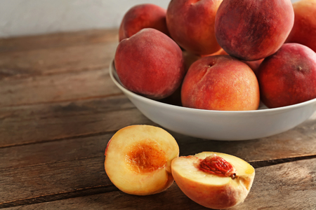 Bowl with fresh peaches on wooden table closeup