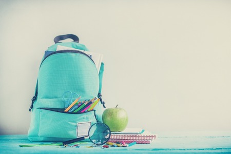 Full turquoise school backpack with stationery on table concept back to school toned image