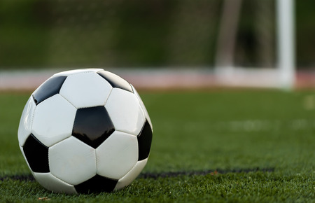 A black and white soccer or football on green field with goal or net in background Stock Photo