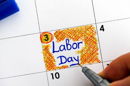 Woman fingers with blue pen writing reminder labor day in calendar close up