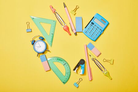 Top view of school supplies scattered on yellow background