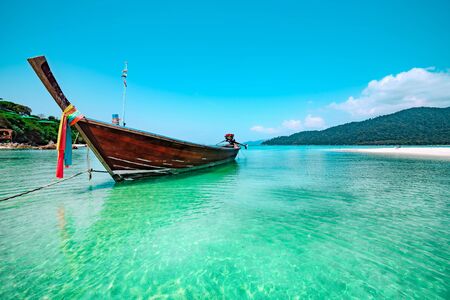 Traditional thai boat moored in sparkling water with reflections of sunlight off a tropical beach in koh lipe thailand in a low angle view on a sunny summer day