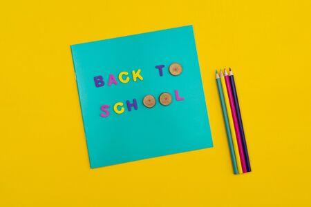 Back to school text on a notepad with colored pencils next to it on orange yellow background letters o replaced with round wooden slices flat lay