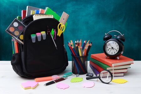 Back to school concept school bag pencils crayons scissor notebooks alarm clock eraser markers watermark ruler pencil sharpener magnifying glass in a combine with a cyan background