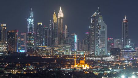 Panorama of the modern arabic city with illuminated skyscrapers and mosque aerial timelapse in financial centre dubai united arab emirates at night