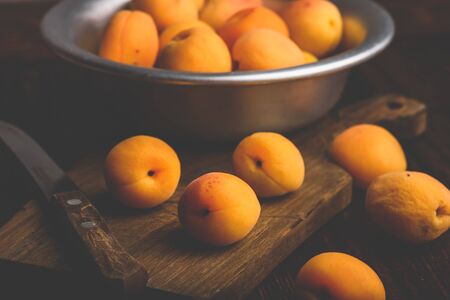 Mellow apricots with knife over old wooden cutting board and metal bowl with fruits Stock Photo