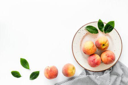 Summer lunch red peaches on white background with tablecloth and leaves top down copy space