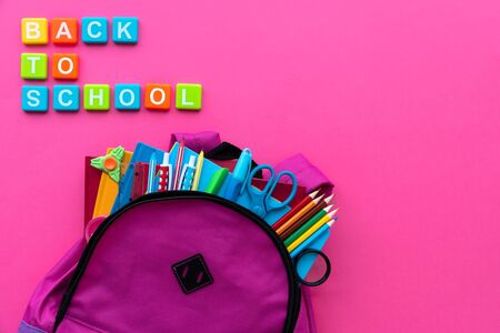 Back to school concept backpack with school supplies and alphabets and numbers blocks on pink background top view copy space