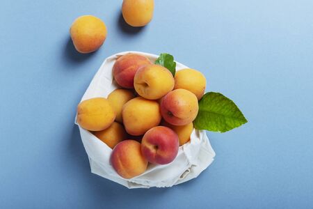 Concept of a biological healthy food and zero waste fresh biological apricots in a cotton shopping bag on a blue background top view image with a copy space Stock Photo