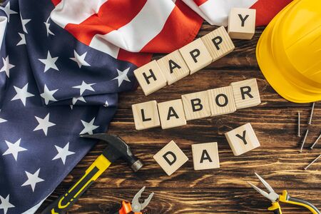 Top view of american flag and instruments near safety helmet and happy labor day lettering on wooden surface