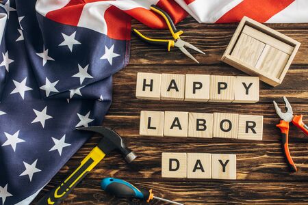 Top view of american flag and instruments near happy labor day lettering on wooden surface