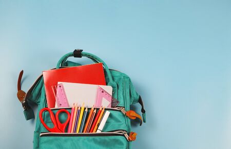 Back to school concept top view of green backpack with school supplies on blue background with copy space Stock Photo