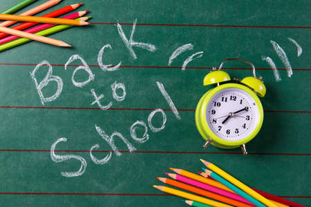 Alarm clock and colored pencils on the chalkboard with back to school text top view Stock Photo