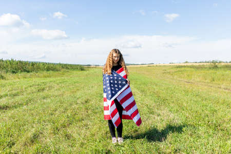 Happy gril with curly hair wrapped in american flag on field labor day usa Stock Photo