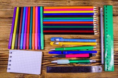 Different school stationeries pens notepad pencils felt tip pens and ruler on wooden background top view