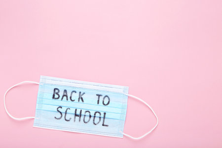 Inscription back to school on medicine mask on pink background