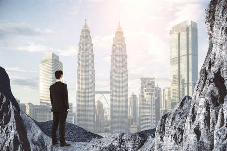 New heights concept with businessman on the rock looking at city skyscrapers in smoke double exposure