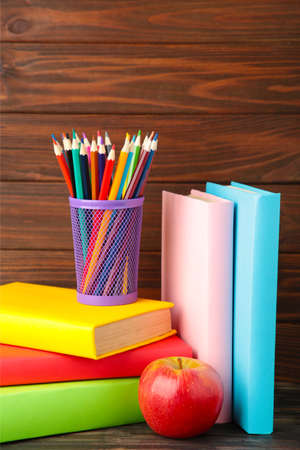 Multi colored school books and stationery on brown wooden background copy space back to school