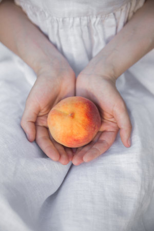 Close up hands of woman farmer holds ripe peaches on linen dress background