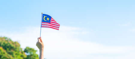 Hand holding malaysia flag on blue sky background september malaysia national day and august independence day