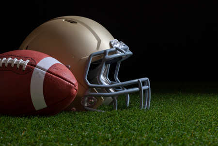 Low angle view of football and gold helmet on grass with dark background