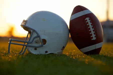 American football and helmet on the field backlit at sunset