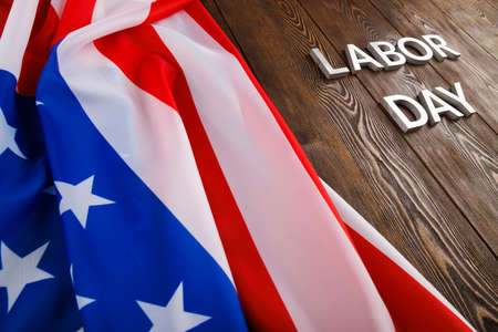 Words labor day laid with silver metal letters on wooden surface with crumpled usa flag on left side in diagonal perspective