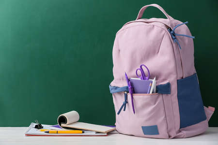 Stylish school backpack with stationery on table against blackboard Stock Photo