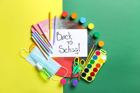 Paper with text back to school paints palette stationery and medical mask on color background Stock Photo