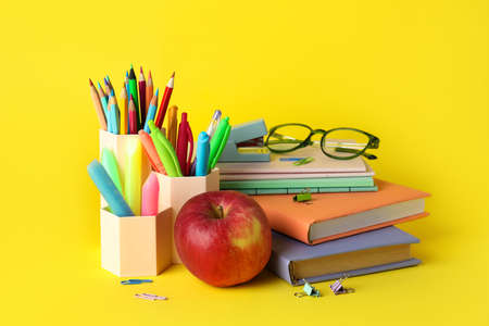 Pen cups with school stationery eyeglasses apple and books on yellow background