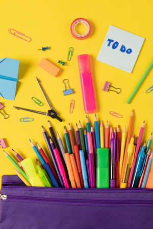 Imagine of various office supplies and plastic utensils notebook crayons on yellow background education learning and creativity Stock Photo