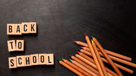 Square wooden letters with the phrase back to school written in english on a black chalkboard background and next to colored pencils Stock Photo