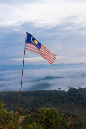 Malaysia flag flying on pole on mountain highland against sea of cloud and blue sky during sunrise Stock Photo