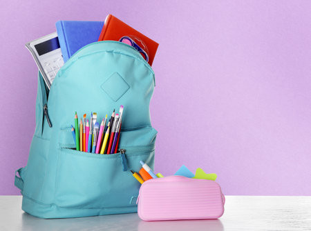 Backpack with school stationery on wooden table against violet background space for text Stock Photo