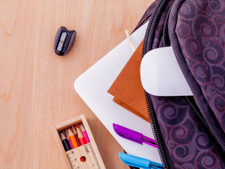 Backpack with school supplies laptop book stationary mouse pen ruler and color pencil on wooden table