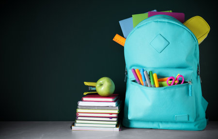 Stylish backpack with different school stationery on table against chalkboard space for text